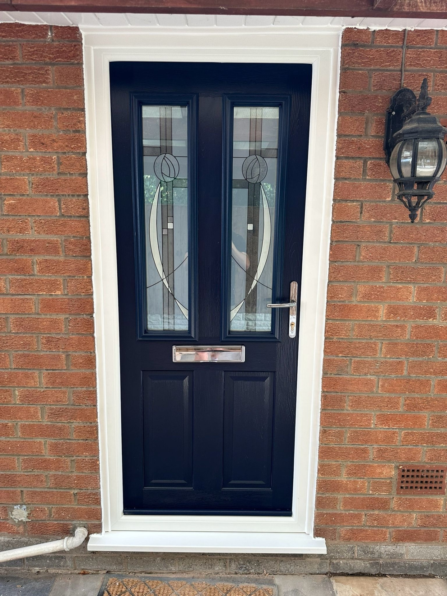 Navy blue composite front door with decorative leaded glass fitted to a red brick home